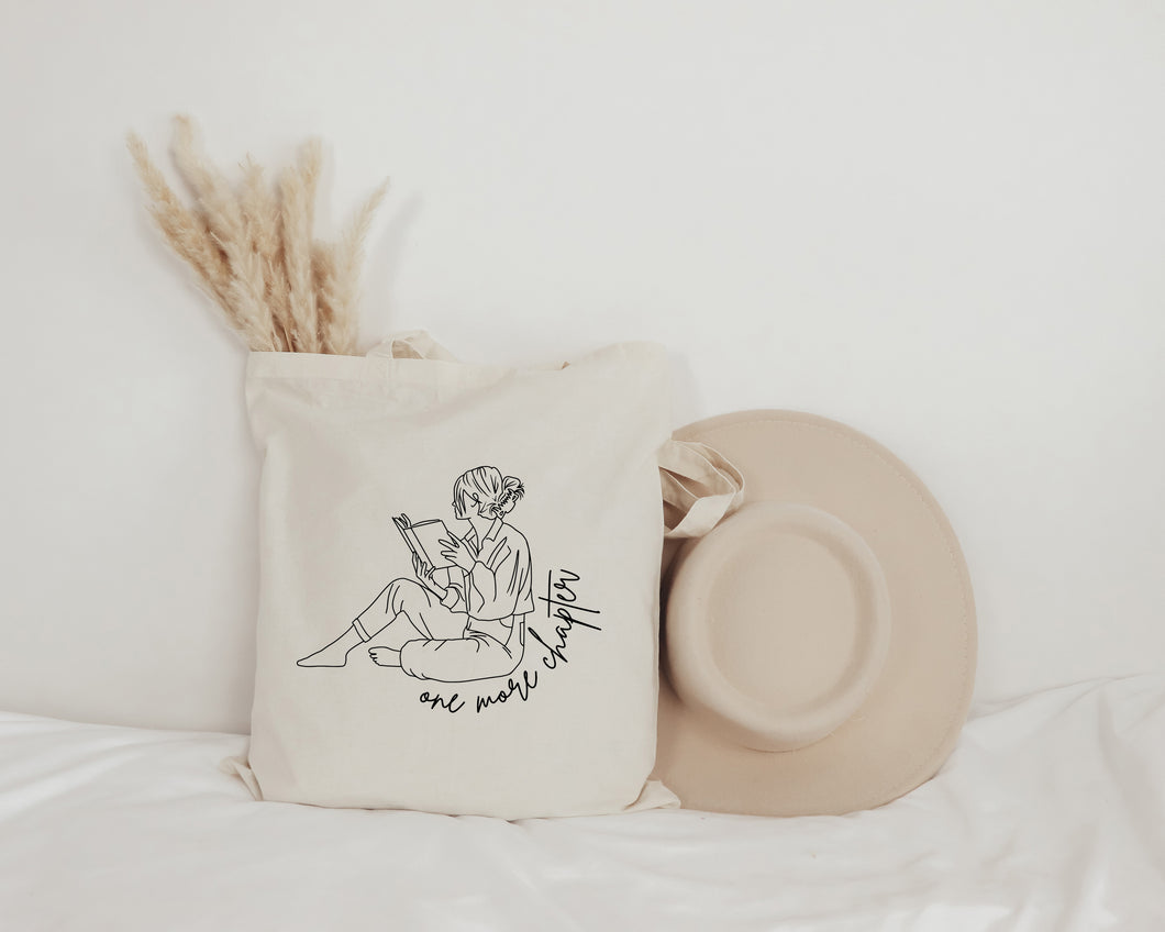 one more chapter tote bag featuring a girl reading a book
